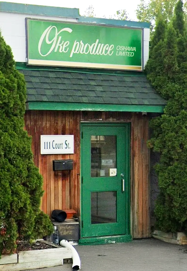 Photo of Oke Produce's storefront. A green door on a wooden building, surrounded by trees
